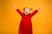 Baby Girl Portrait Isolate Yellow Background.Stylish Little Baby With Hands Up. Portrait Of Shocked Little Girl In Red Dress Isolated On Yellow Background 