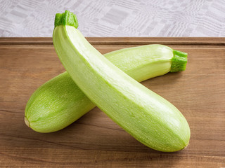 Two fresh green courgettes or zucchini criss-cross on a brown wooden cutting board. Cook at home. Fresh vegetables, vegetarianism and healthy eating.