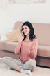 © LIGHTFIELD STUDIOS - beautiful smiling woman sitting on carpet, talking on smartphone and gesturing at home