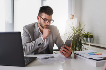 Businessman sitting on his office desk working on a computer and using smart phone