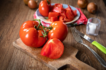 Wall Mural - Whole and sliced tomatoes on cutting board and ceramic plate and whole onion in the background. Old wooden table.