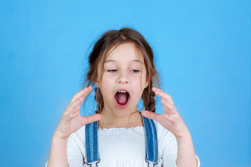 Emotional portrait little beautiful girl with pigtails in jeans overalls eating bites holding an apple. 6-7 years studio