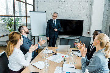 Wall Mural - selective focus of business coach standing near white board near multicultural coworkers clapping hands in conference room