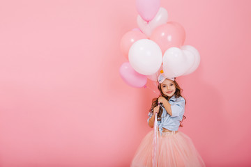 Wall Mural - Happy celebration of birthday party with flying balloons of charming cute little girl in tulle skirt smiling to camera isolated on pink background. Charming smile, expressing happiness. Place for text
