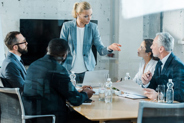 Wall Mural - selective focus of business coach talking and gesturing in conference room near multicultural coworkers