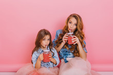 Mom And Daughter In Vintage Clothes Prepared Tasty Berry Fresh And Drink It From Big Glass Jars Sitting On The Floor. Little Curly Girl Posing With Her Adorable Mother Holding Glass Of Cherry Cocktail