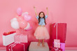 © Look! - Excited young girl in tulle skirt having fun to camera isolated on pink background. Enjoying a lot of big presents, colorful balloons, celebrating happy birthday party of pretty princess