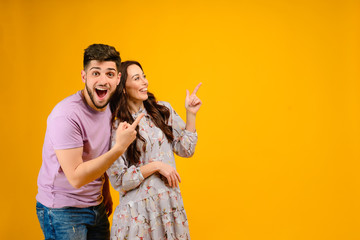 Photo of young couple man and woman smiling pointing at copyspace isolated over yellow background