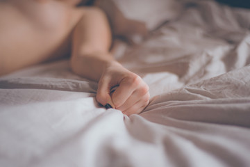 Hand sign orgasm of woman on white bed. Hand of female pulling white sheets in ecstasy. Feeling and emotion concept. Love sex concept.