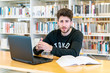© ALEJANDRO - Young green-eyed student sitting in front of laptop with books at the table looking confused in the library