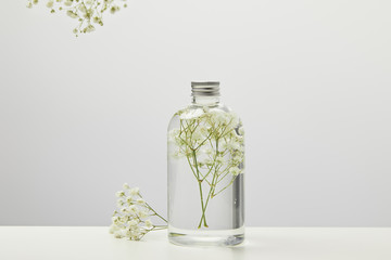 organic beauty product in transparent bottle with white wildflowers on grey background