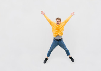 Wall Mural - Happy guy in Casual clothes jumps against the background of a white wall, street portrait. Young man is leap on the background of a white wall,jumping on the street, isolated. Copyspace