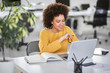 © nenadaksic - Smiling mixed race businesswoman holding eyeglasses and looking at laptop while sitting in modern office.