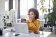 © nenadaksic - Serious mixed race businesswoman dressed casual sitting in modern office and using laptop.