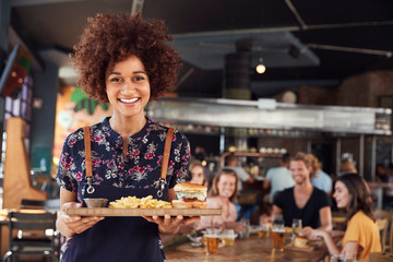 Portrait Of Waitress Serving Food To Customers In Busy Bar Restaurant