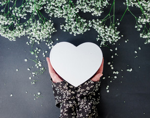 Female hands holding heart shape gift box near Gypsophila paniculata flowers