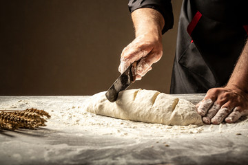 Baker making patterns on raw bread using a knife to shape the dough prior to baking. Manufacturing process of spanish bread. Food concept