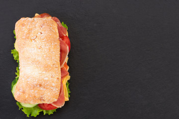 Ciabatta sandwich with lettuce , prosciutto and  cheese over stone background. Top view with copy space