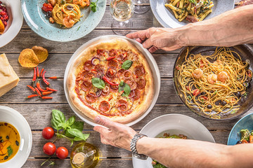 Pizza salami in cook hands. Chef serving pizza diavolo in the middle table full of italian meals