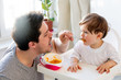 © Masson - Young father try to feeding a toddler boy with a spoon in a chair