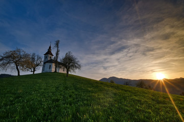 Wall Mural - St.Tomas church near Skofja Loka in sunest with spring grass