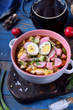 Russian cold soup Okroshka with vegetables, sausage, eggs and kvass in a ceramic bowl on the blue table