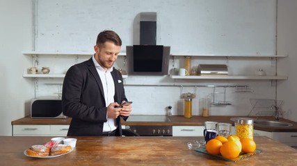 Young attractive businessman wearing suit checks the news. Caucasian guy stands in cozy kitchen.
