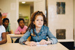© Maskot - Portrait of smiling schoolgirl sitting with friends at desk in classroom