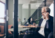 © Maskot - Mature male manager talking on mobile phone seen through glass wall at creative office