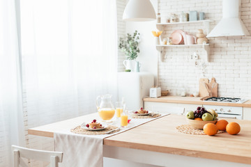 served table with pancakes, fruits and orange juice in kitchen