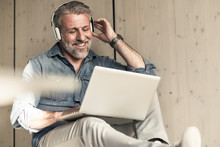 Casual mature businessman sitting down with laptop and headphones