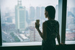 © Maridav - Businesswoman drinking coffee at work contemplative looking out the window of high rise skyscraper building during morning tea break. Stress, mental health in the workplace. Career job concept.