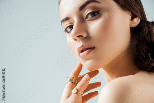 young naked woman with shiny makeup and golden rings touching chin and ...