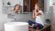 © alexeg84 - Little cute girl brushes her teeth with dental floss while sits on the table near the sink at domestic bathroom in front of the mirror.