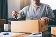 © wutzkoh - Asian entrepreneur teenagers are using the tape to seal the box by packing the product to send to customers.