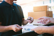 © wutzkoh - Young asian man smiling while delivering a cardboard box to the woman holding document to signing signature.