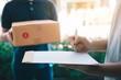 © wutzkoh - Delivery young man standing at the door of home and carrying parcels for young male to signing.