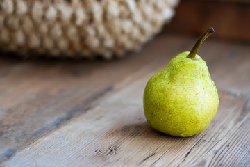 one fresh ripe organic yellow pear on rustic wooden brown table with defocused pears in basket on background. Selective focus. Horizontal copy space For design about agricilture, fruit, healthy food