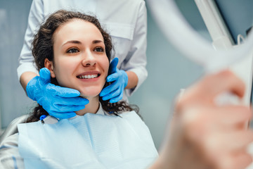 Wall Mural - A woman is sitting at a dentist's reception. She looks in the mirror at her teeth. A dentist is sitting next to each other. Woman smiling. Happy patient and dentist concept.