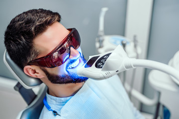 dentist starting teeth whitening procedure with young man.