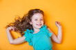 Cute 7 old girl in blue blouse lying on orange background
