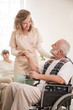 Senior man on wheelchair with helpful nurse holding his hand