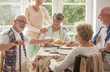 © Photographee.eu - Group of senior friends with helpful carer sitting together at the table at nursing home dining room and eating cake