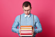 © sementsova321 - Indoor studio shot of dark haired confused model posing isolated over bright pink background, holding books in his strong hands, looking at them, reading text and assignments. Youth and study concept.