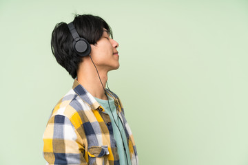 Asian man over isolated green wall listening to music with headphones