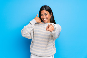 Wall Mural - Young Colombian girl with sweater making phone gesture and pointing front