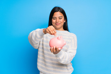 Wall Mural - Young Colombian girl with sweater taking a piggy bank and happy because it is full