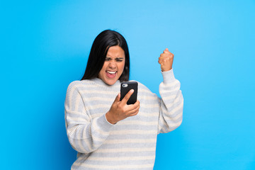 Wall Mural - Young Colombian girl with sweater celebrating a victory with a mobile