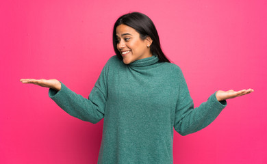 Wall Mural - Young Colombian girl with green sweater holding copyspace with two hands