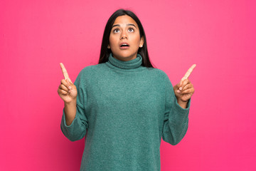 Wall Mural - Young Colombian girl with green sweater surprised and pointing up